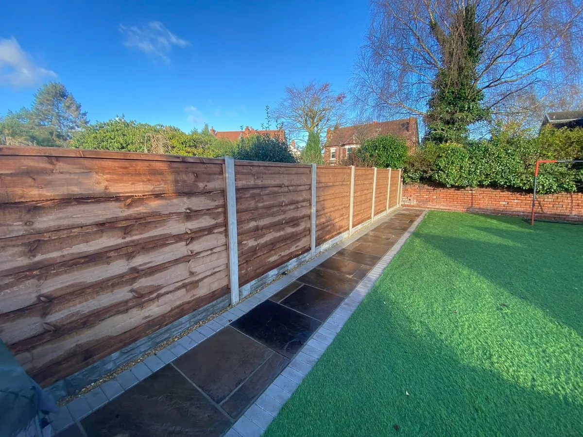 Finished dark-stained feather-edge fence panels alongside a paved garden path and artificial lawn